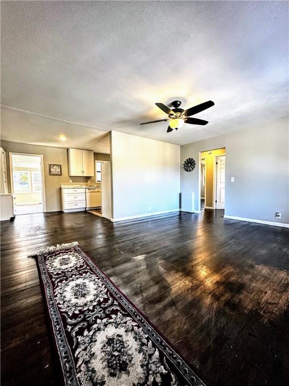 unfurnished living room with a textured ceiling, dark wood-type flooring, a ceiling fan, and baseboards