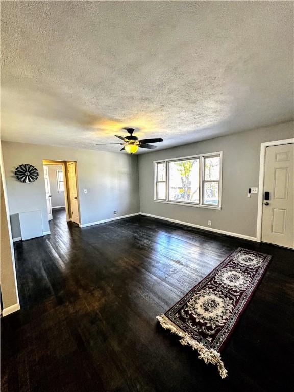 unfurnished living room with a ceiling fan, a textured ceiling, baseboards, and dark wood-type flooring