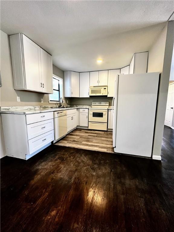 kitchen with white appliances, white cabinets, dark wood-style floors, light countertops, and a sink