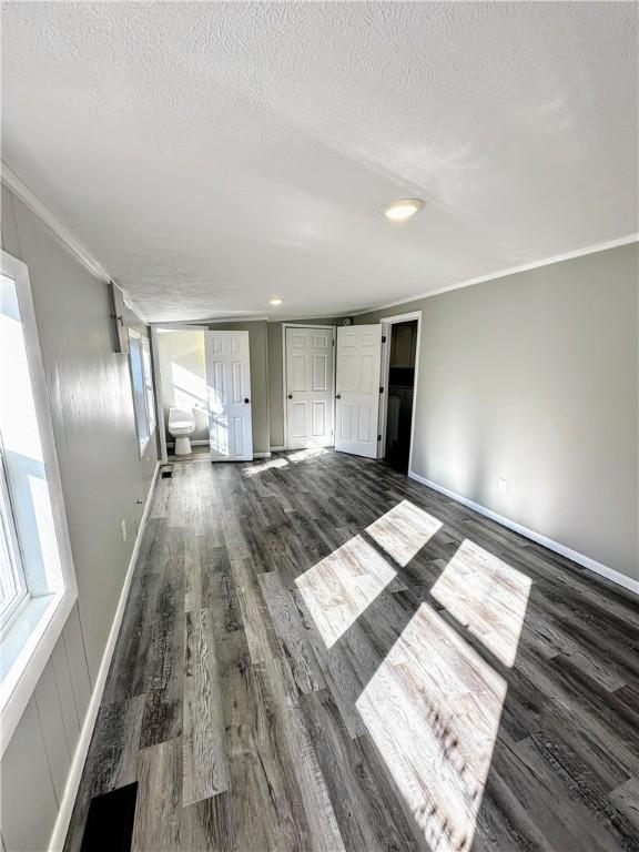 unfurnished living room with crown molding, a textured ceiling, baseboards, and dark wood-style flooring