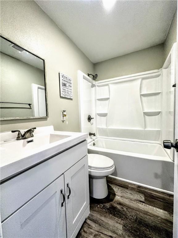 full bath with shower / bathtub combination, a textured ceiling, toilet, wood finished floors, and vanity