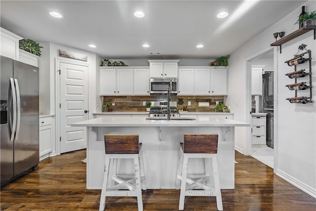 kitchen with dark wood-type flooring, appliances with stainless steel finishes, white cabinets, and an island with sink