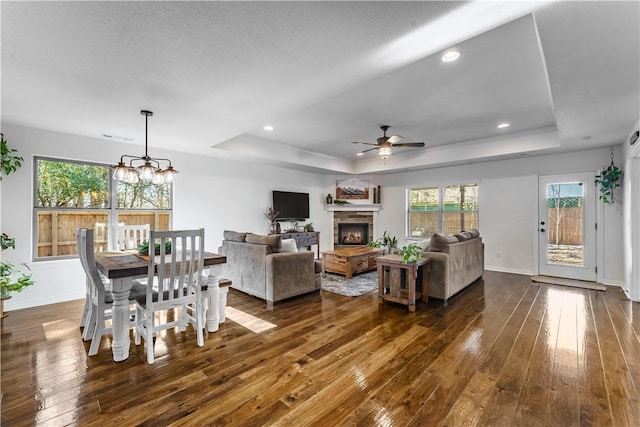 living room with ceiling fan with notable chandelier, dark hardwood / wood-style flooring, a raised ceiling, and a fireplace