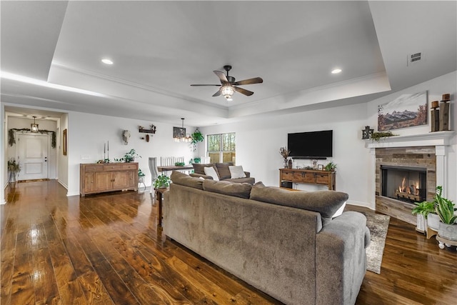 living room with a raised ceiling, ceiling fan, dark hardwood / wood-style floors, and a stone fireplace