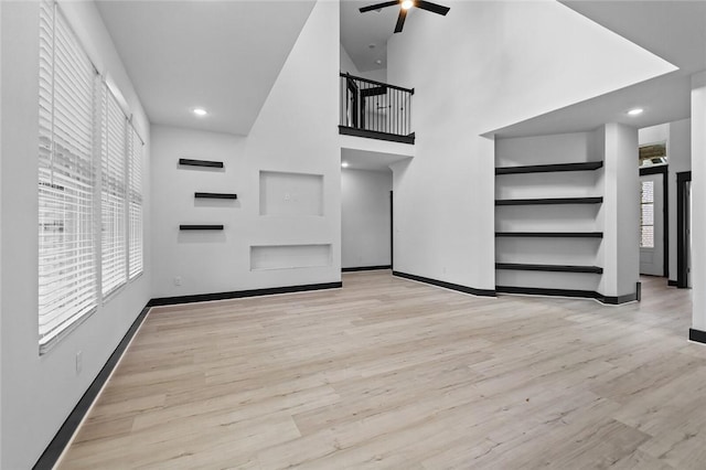 unfurnished living room featuring ceiling fan, a towering ceiling, and light hardwood / wood-style flooring