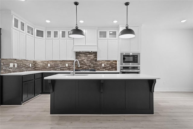 kitchen featuring stainless steel oven, built in microwave, pendant lighting, and a center island with sink