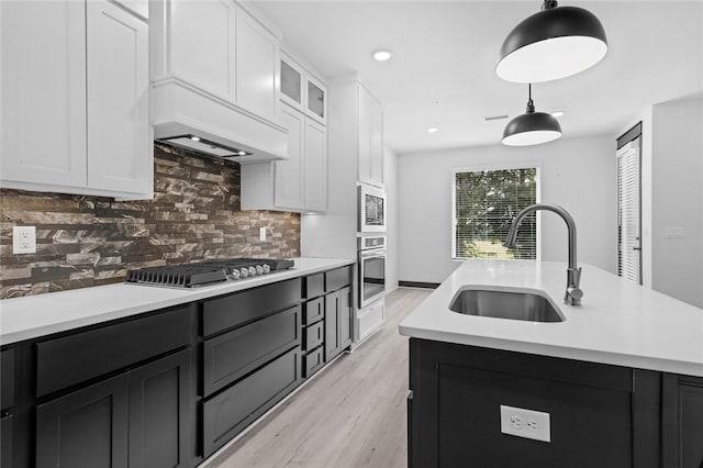 kitchen with decorative light fixtures, sink, appliances with stainless steel finishes, an island with sink, and white cabinets