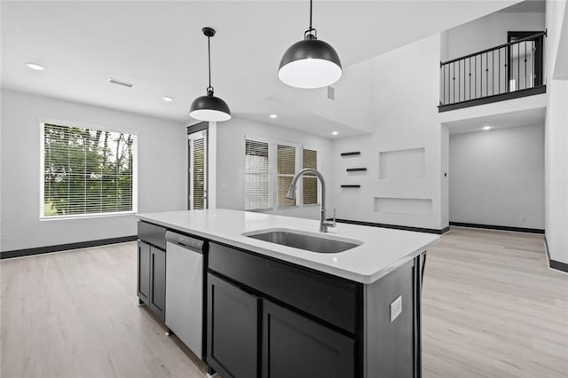 kitchen with light hardwood / wood-style floors, a center island with sink, hanging light fixtures, stainless steel dishwasher, and sink