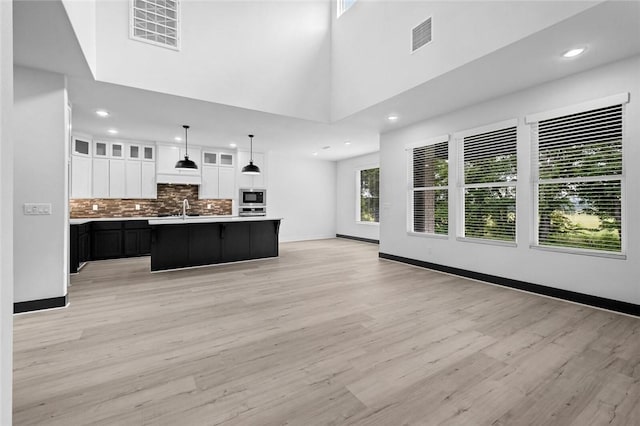 kitchen featuring pendant lighting, light hardwood / wood-style floors, a center island with sink, a towering ceiling, and white cabinets