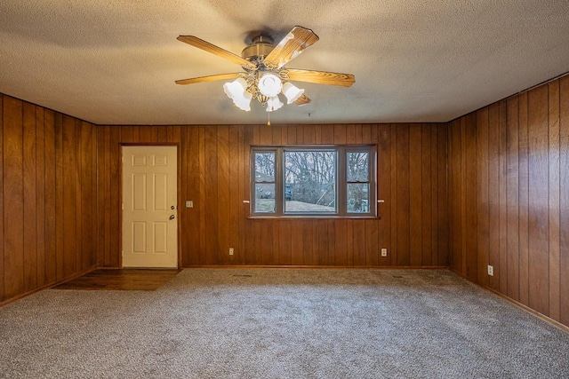 unfurnished room featuring wood walls, ceiling fan, a textured ceiling, and carpet floors