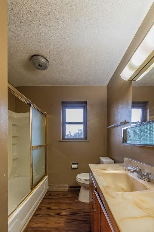 full bathroom with toilet, bath / shower combo with glass door, wood-type flooring, a textured ceiling, and vanity