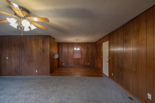 unfurnished living room with ceiling fan, wood walls, a textured ceiling, and dark colored carpet