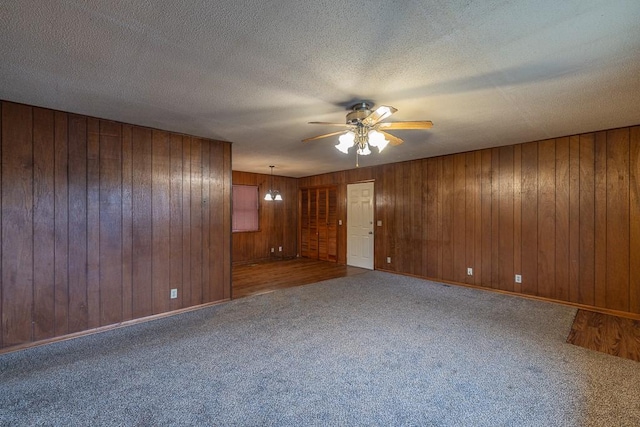 spare room featuring ceiling fan with notable chandelier, carpet, wood walls, and a textured ceiling