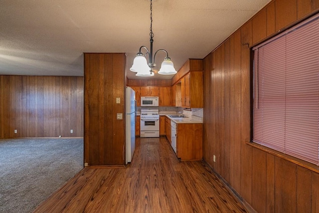 kitchen with pendant lighting, sink, wooden walls, an inviting chandelier, and white appliances