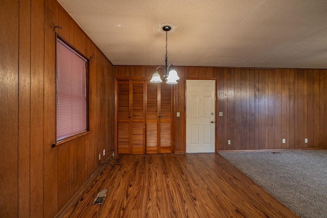 unfurnished dining area featuring wooden walls, an inviting chandelier, and a textured ceiling