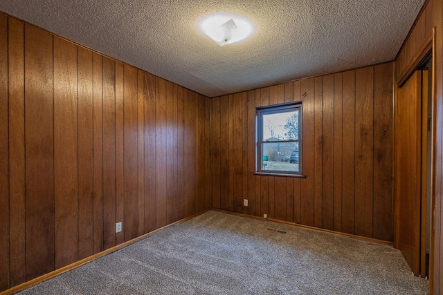 carpeted empty room with wooden walls and a textured ceiling