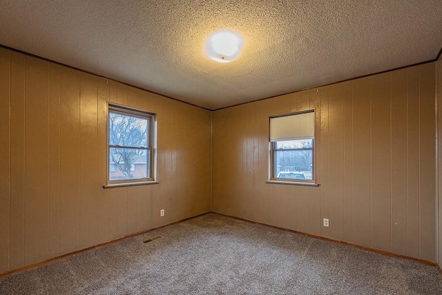 carpeted empty room with a textured ceiling and wood walls