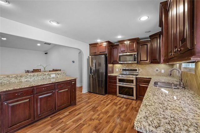 kitchen featuring decorative backsplash, wood-type flooring, sink, stainless steel appliances, and light stone counters