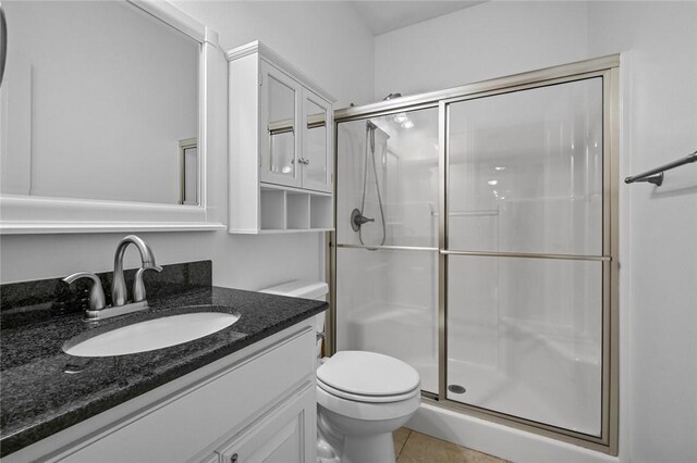 bathroom with a shower with shower door, toilet, vanity, and tile patterned flooring