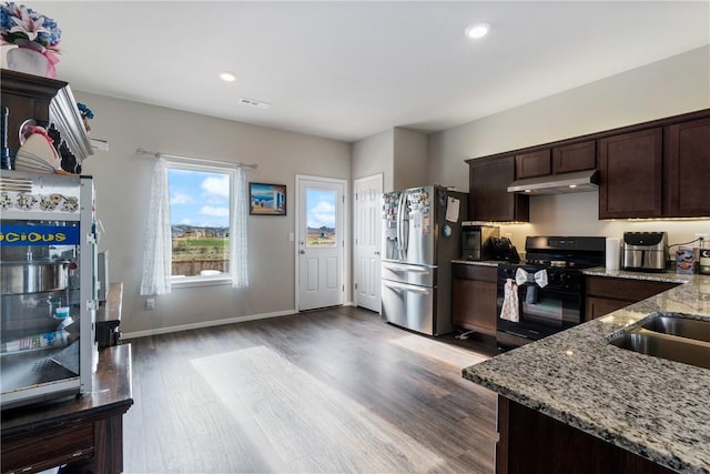 kitchen featuring under cabinet range hood, dark brown cabinets, light stone countertops, gas stove, and stainless steel fridge