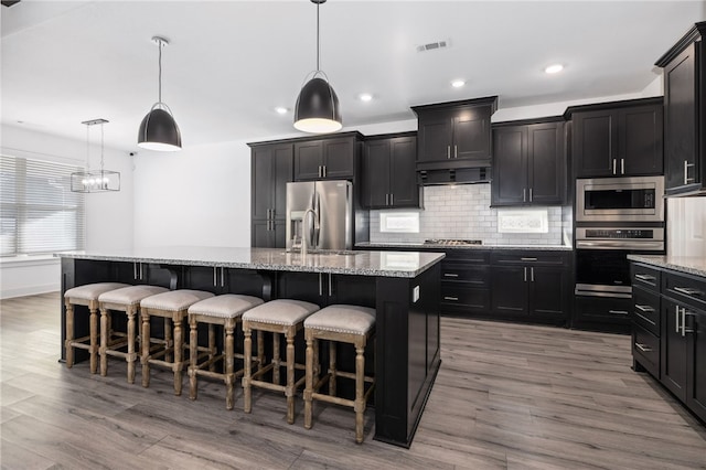 kitchen featuring a breakfast bar, a kitchen island with sink, appliances with stainless steel finishes, and pendant lighting