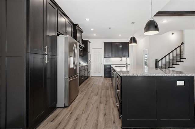 kitchen featuring a center island with sink, stainless steel refrigerator with ice dispenser, sink, hanging light fixtures, and light wood-type flooring