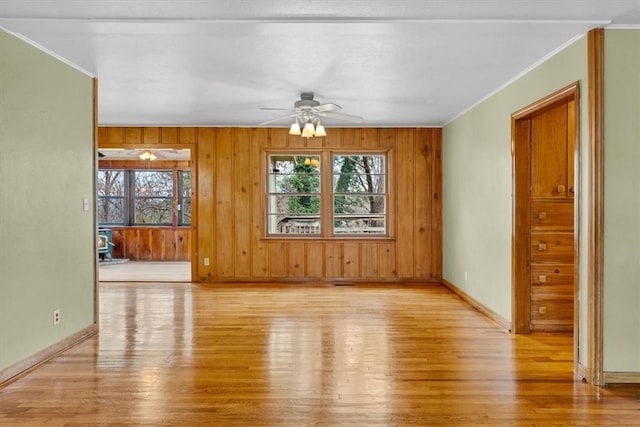 spare room with ceiling fan, ornamental molding, light hardwood / wood-style floors, and wooden walls