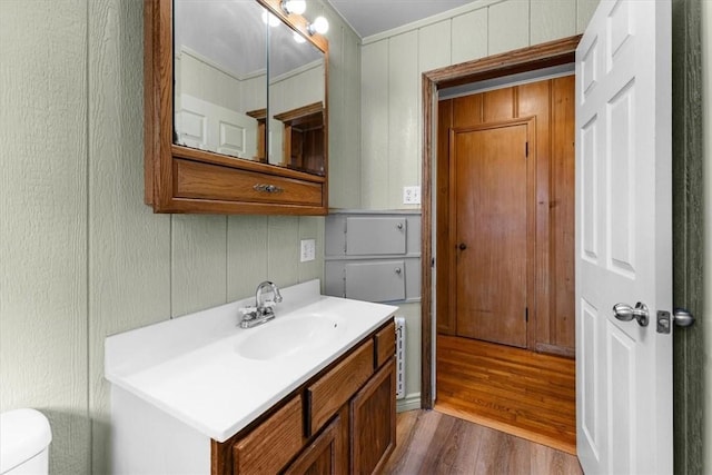 bathroom featuring wood-type flooring, toilet, vanity, and ornamental molding