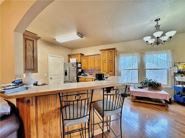 kitchen featuring arched walkways, hardwood / wood-style flooring, brown cabinets, stainless steel fridge, and a kitchen bar