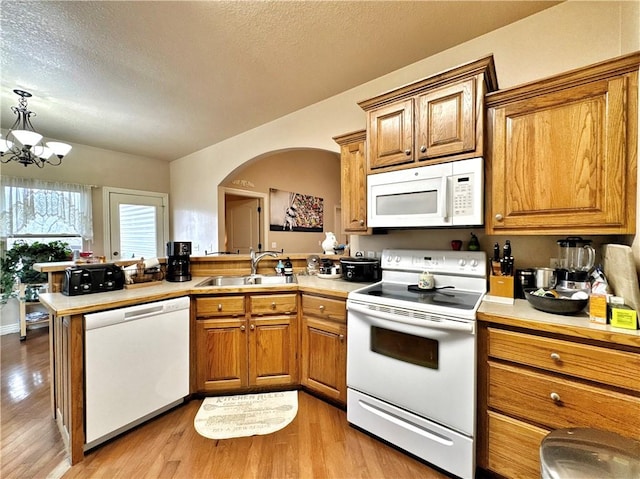 kitchen with white appliances, wood finished floors, a sink, light countertops, and brown cabinetry