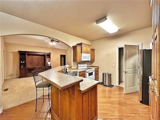 kitchen featuring white appliances, arched walkways, brown cabinets, a peninsula, and a sink