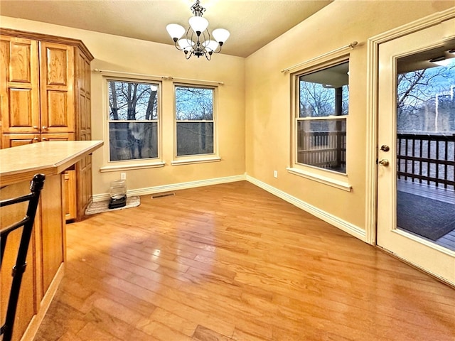 unfurnished dining area with an inviting chandelier, baseboards, visible vents, and light wood finished floors