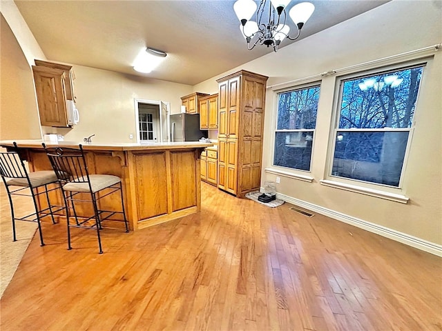 kitchen featuring light wood-style floors, a breakfast bar area, freestanding refrigerator, and brown cabinets