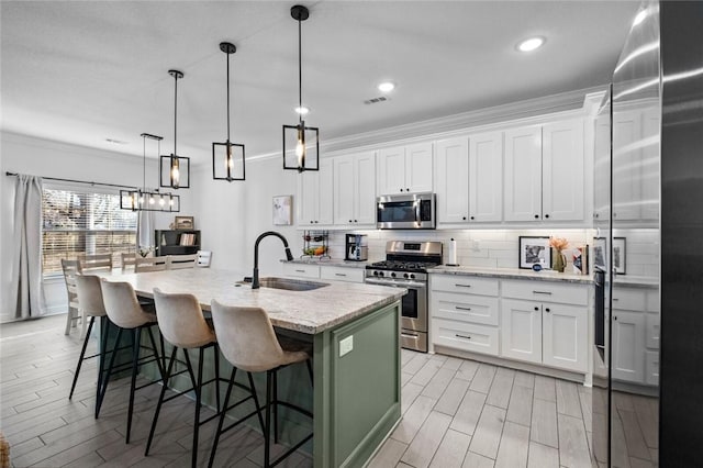 kitchen with stainless steel appliances, a kitchen island with sink, light stone countertops, white cabinets, and sink