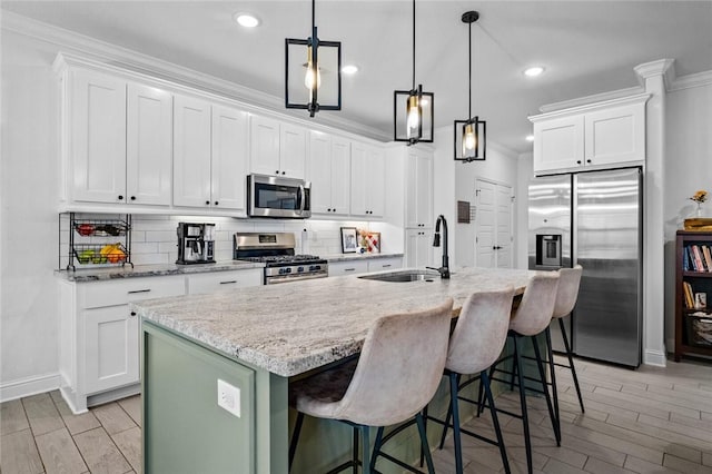 kitchen featuring white cabinets, a kitchen island with sink, appliances with stainless steel finishes, and a kitchen breakfast bar