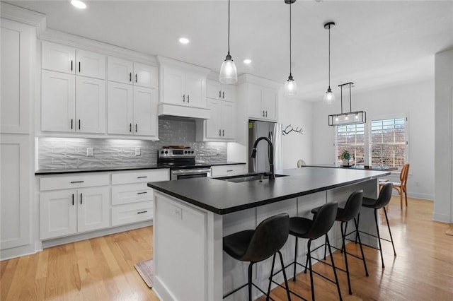 kitchen with stainless steel appliances, pendant lighting, white cabinets, and a center island with sink