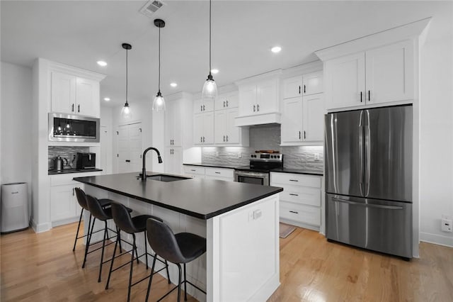 kitchen with pendant lighting, a center island with sink, sink, white cabinetry, and appliances with stainless steel finishes