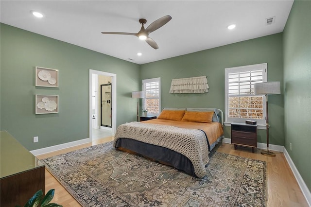 bedroom featuring ceiling fan, connected bathroom, multiple windows, and light hardwood / wood-style floors