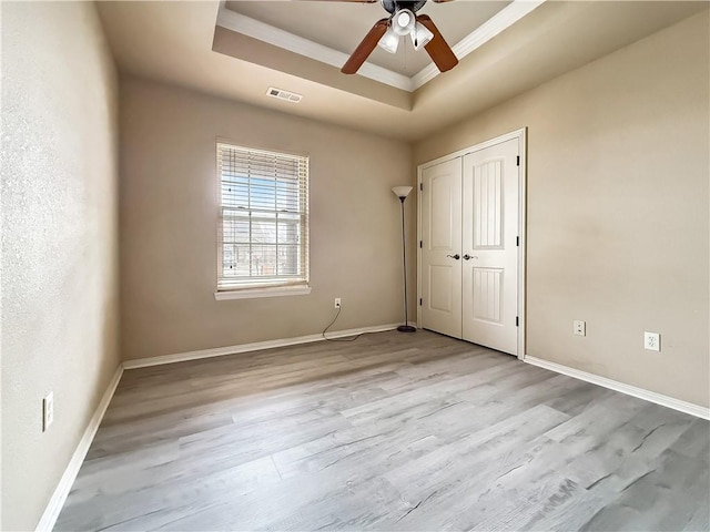 unfurnished room with light hardwood / wood-style floors, a tray ceiling, crown molding, and ceiling fan