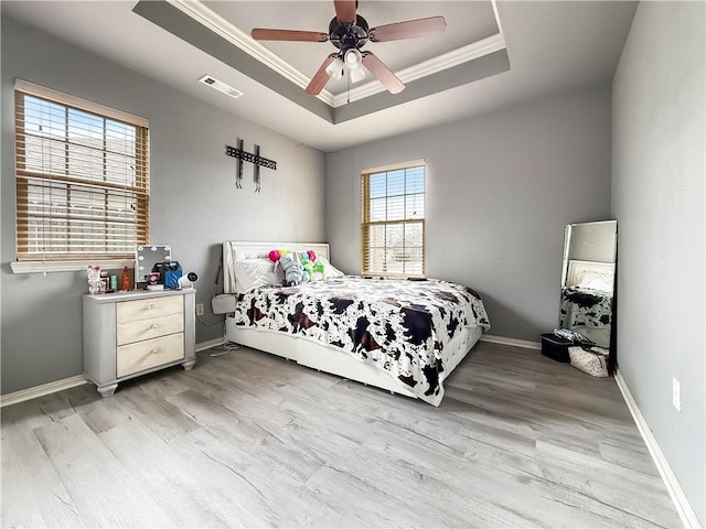 bedroom featuring light wood-type flooring, ceiling fan, crown molding, and a tray ceiling