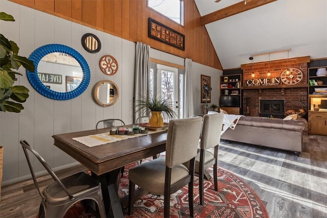 dining space with wooden walls, dark wood-type flooring, built in shelves, high vaulted ceiling, and beamed ceiling