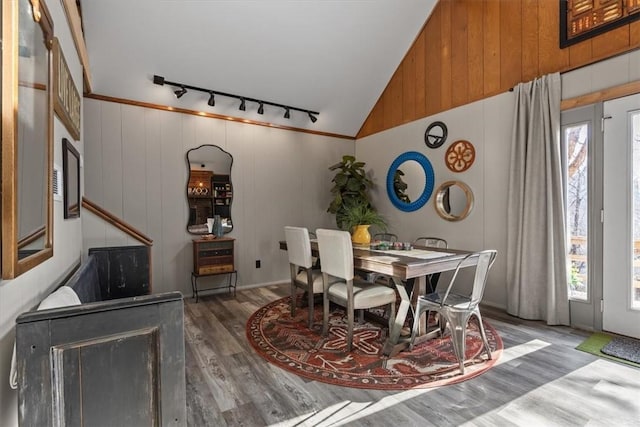 dining room with lofted ceiling, rail lighting, hardwood / wood-style floors, and wooden walls