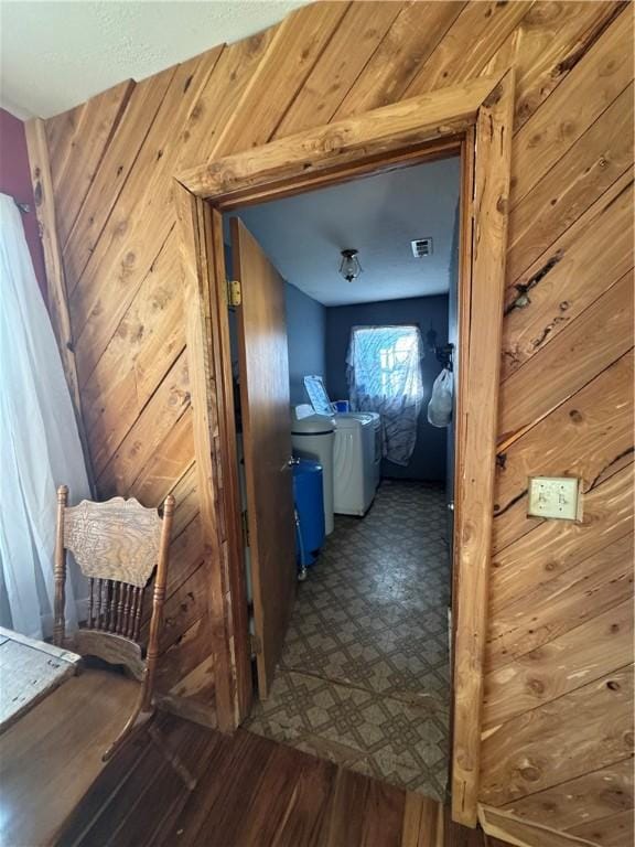 hallway with wood-type flooring, washing machine and clothes dryer, and wooden walls