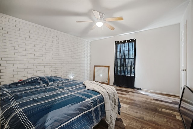 bedroom featuring ceiling fan, brick wall, and wood-type flooring