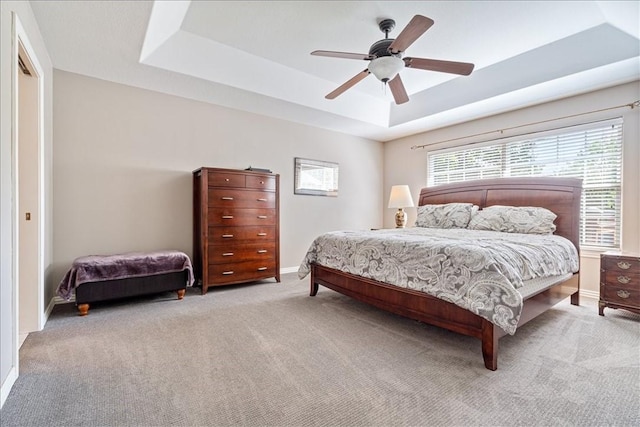 bedroom with a raised ceiling, ceiling fan, and light carpet