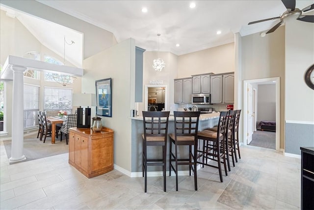 kitchen featuring a towering ceiling, ornate columns, a kitchen breakfast bar, gray cabinets, and crown molding