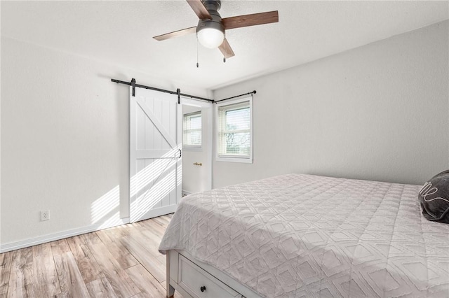 bedroom with ceiling fan, a barn door, and light wood-type flooring