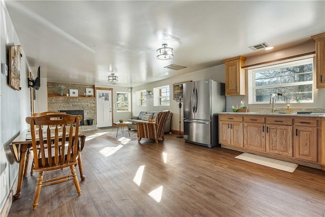 kitchen with wood-type flooring, stainless steel fridge, plenty of natural light, and a stone fireplace