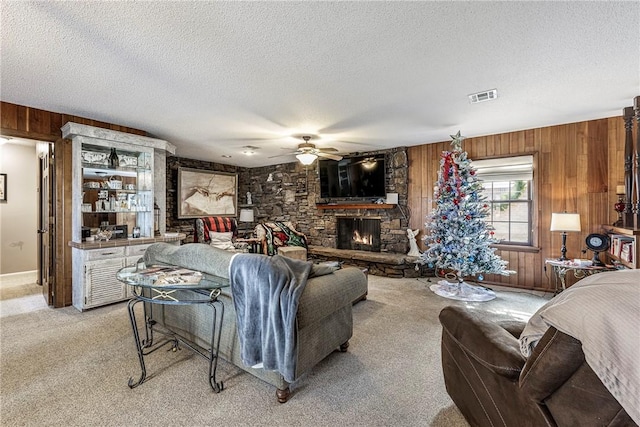 carpeted living room with ceiling fan, a fireplace, a textured ceiling, and wood walls