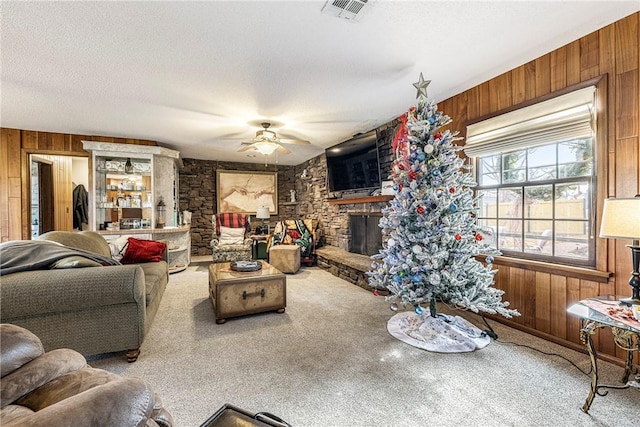 living room with ceiling fan, wooden walls, carpet floors, a fireplace, and a textured ceiling